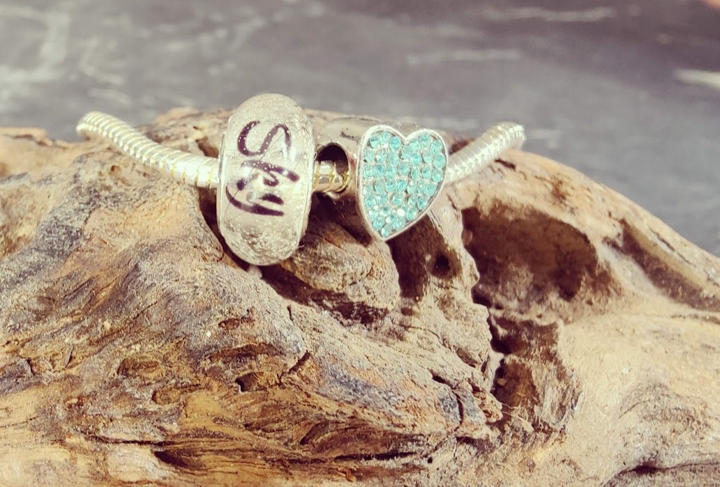 Sterling Silber Armband mit Fellperle mit Name und türkisem Strass-Herzanhänger auf Treibholz, Nahaufnahme – personalisierter Gedenkschmuck von Zinou Minimanufaktur