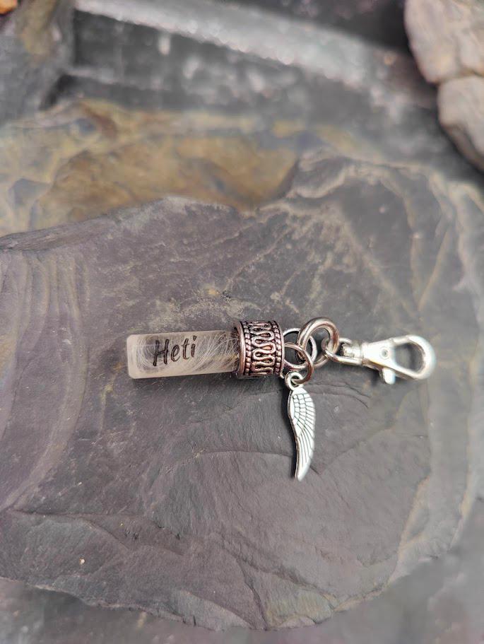 Stäbchen-Amulett mit grauem Tierhaar und silberner Zierfassung mit Flügelcharm  und der Name Heti Tierhaarschmuck von Zinou Minimanufaktur