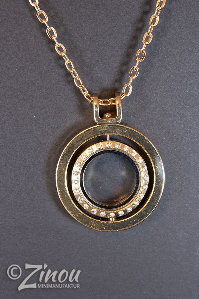 Statement Kette mit goldenem Medaillon und leerem Glasfach, Frontansicht auf grauem Hintergrund – Zinou Minimanufaktur