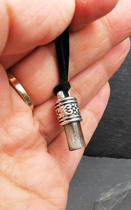 Stäbchen-Amulett mit grauem Tierhaar und silberner Zierfassung mit Om-Symbol in einer Handfläche gehalten, Nahaufnahme – Tierhaarschmuck von Zinou Minimanufaktur