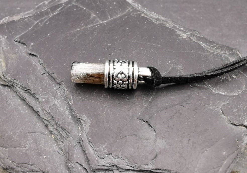 Stäbchen-Amulett mit hellem Tierhaar und silberner Zierfassung mit Herzornament an schwarzer Kordel auf Schieferstein, Nahaufnahme – Tierhaarschmuck von Zinou Minimanufaktur