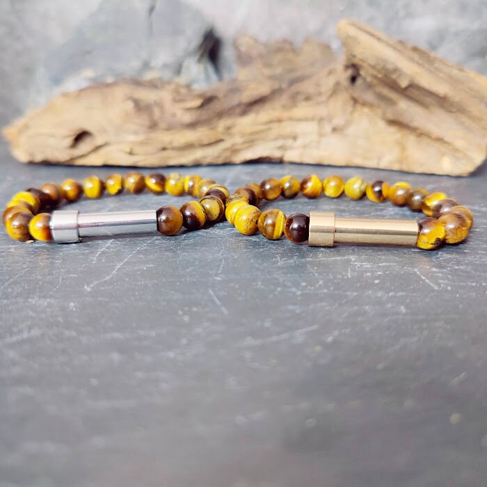 Zwei Tigerauge-Armbänder mit Miniurnen-Zylinder in Silber und Gold im Vergleich auf Schieferstein – Gedenkschmuck von Zinou Minimanufaktur