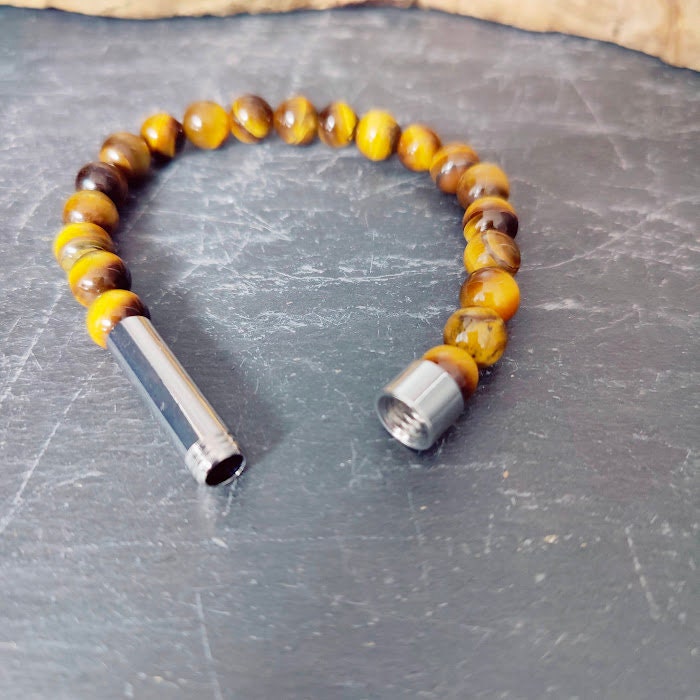 Tigerauge-Armband mit geöffnetem Miniurnen-Zylinder auf Schieferstein, Innenraum zum Befüllen sichtbar – Gedenkschmuck von Zinou Minimanufaktur