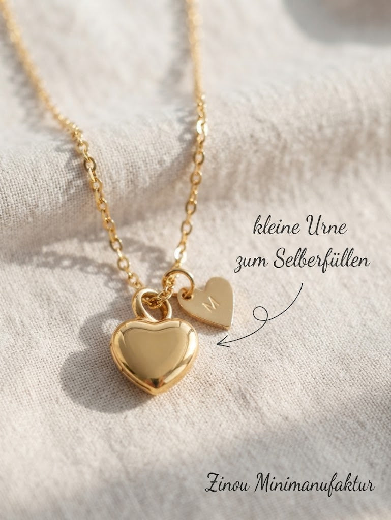goldene Urne aus Edelstahl liegt auf einem hellen Stoff und es steht kleine Urne zum Selberfüllen mit Pfeil auf das goldene Herz