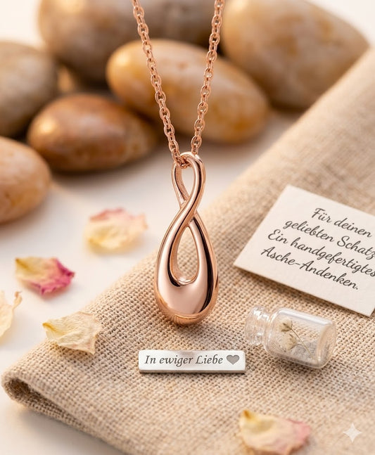 Roségoldener Infinity-Urnenanhänger an Roségoldkette auf Leinentuch mit Steinen, getrockneten Blüten und Geschenkkärtchen – Gedenkschmuck zum selber Füllen von Zinou Minimanufaktur