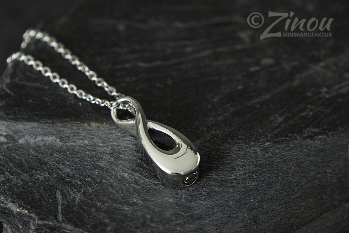 Silberner Infinity-Urnenanhänger an Silberkette liegend auf dunklem Schieferstein, Draufsicht – Gedenkschmuck von Zinou Minimanufaktur