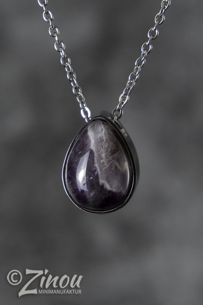 Silberner Tropfen-Urnenanhänger mit violettem Amethyst-Halbedelstein an Silberkette hängend vor grauem Hintergrund – Gedenkschmuck von Zinou Minimanufaktur