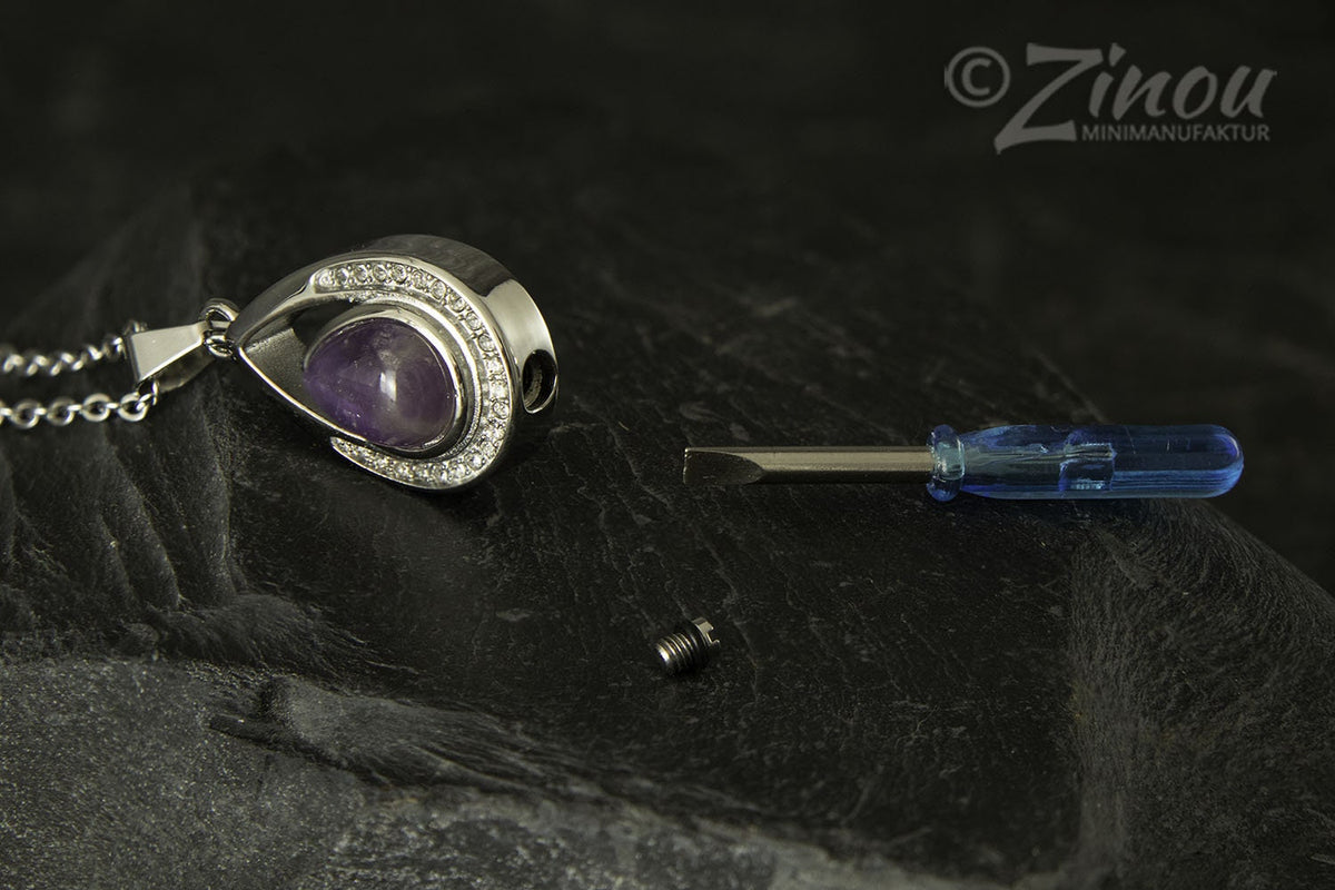 Silberner Tropfen-Urnenanhänger mit Amethyst geöffnet auf Schieferstein, daneben Schraube und Minischraubenzieher zum Befüllen – Gedenkschmuck von Zinou Minimanufaktur