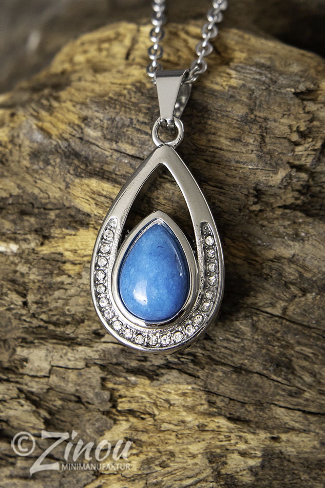 Silberner Tropfen-Urnenanhänger mit blauem Halbedelstein und Strasssteinen hängend an Silberkette auf Holz – Gedenkschmuck von Zinou Minimanufaktur
