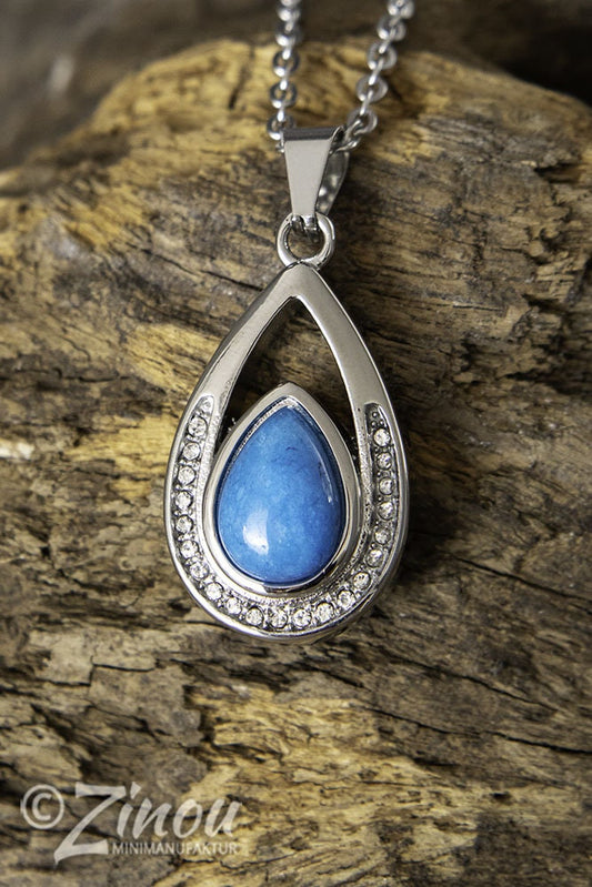 Silberner Tropfen-Urnenanhänger mit blauem Halbedelstein und Strasssteinen hängend an Silberkette auf Holz – Gedenkschmuck von Zinou Minimanufaktur