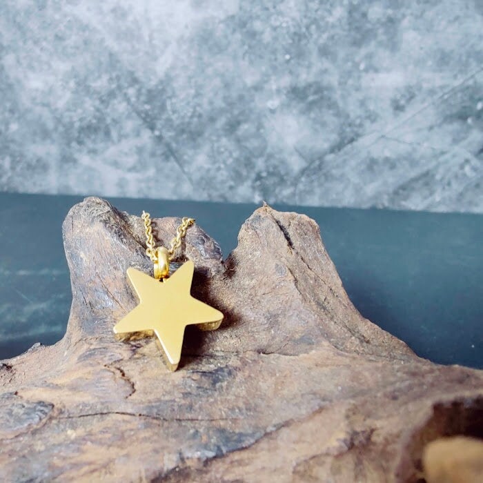 Goldener Stern-Anhänger Urnenschmuck mit Kette auf Treibholz vor blauem Hintergrund – Zinou Minimanufaktur