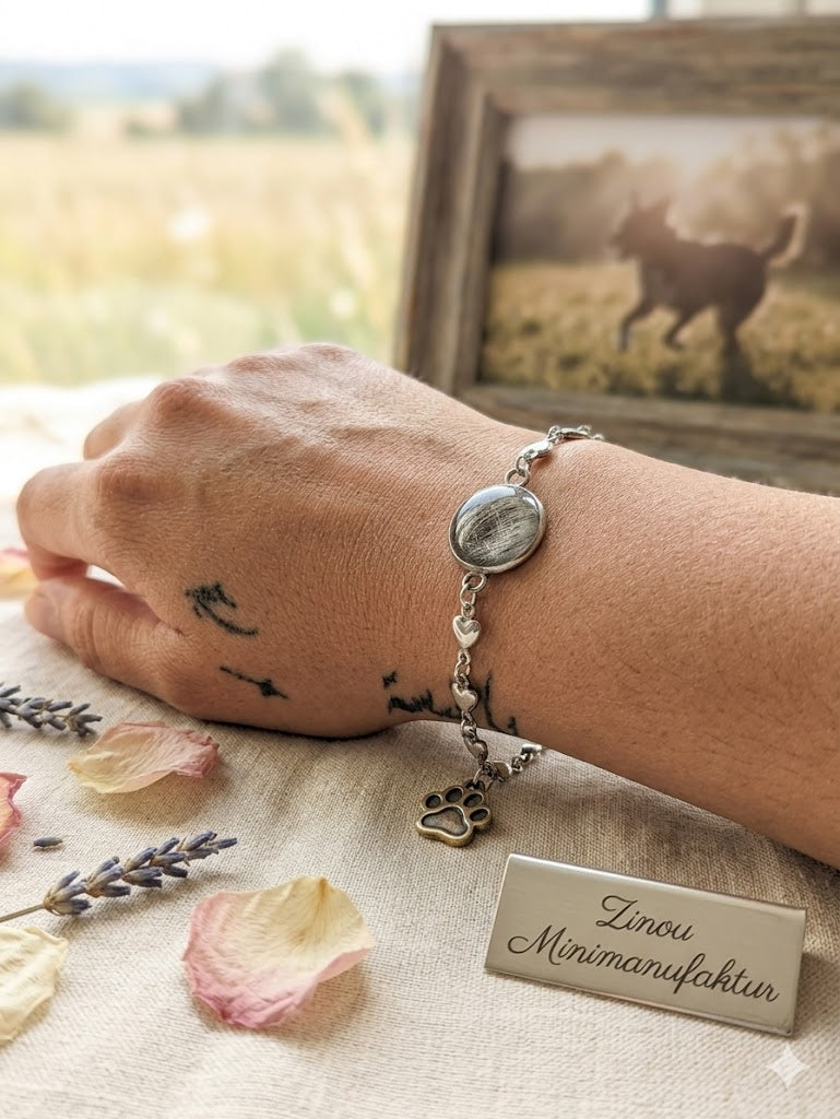 Arm mit einem Edelstahl Armband gefüllt mit Fell liegt auf dem Tisch im Hintergrund ein Foto von einem schwarzen Hund