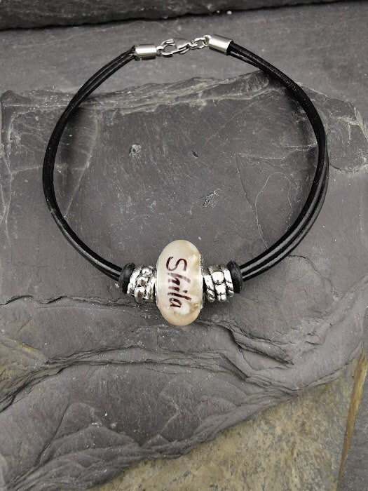 Schwarzes Lederarmband Lenni mit weißer Fellperle und graviertem Namen „Shila\" auf Schieferstein – Tierhaarschmuck von Zinou Minimanufaktur